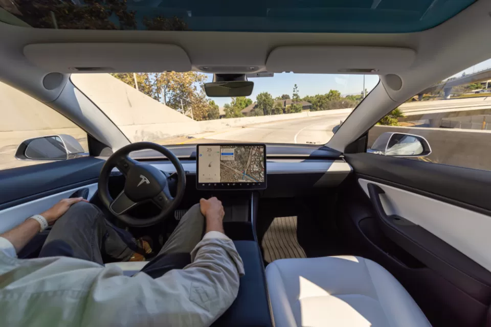 Interior of Tesla car with driver holding hands off wheel in 'full self-driving' mode